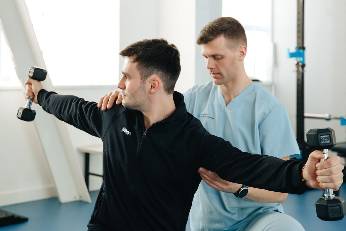 A physiotherapist supporting a patient during a shoulder strengthening exercise with a dumbbell